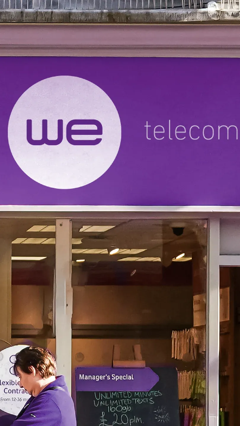 WE storefront with a purple fascia, white circular logo and glass entrance