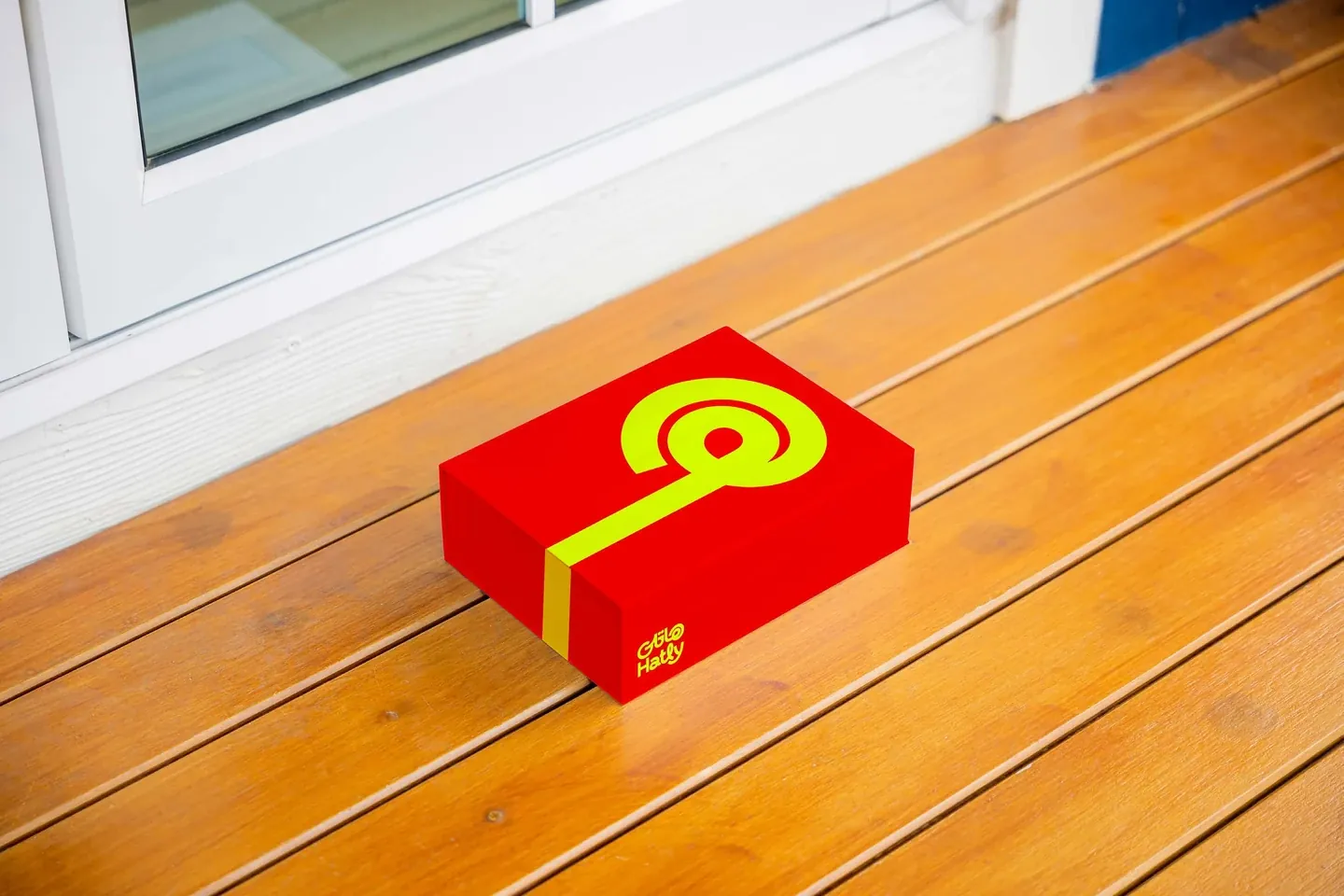 Hatly red delivery box with lime road-shaped symbol on a wooden doorstep