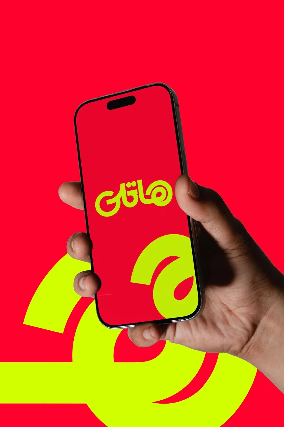 Hand holding a phone with the Arabic Hatly app opening screen on red