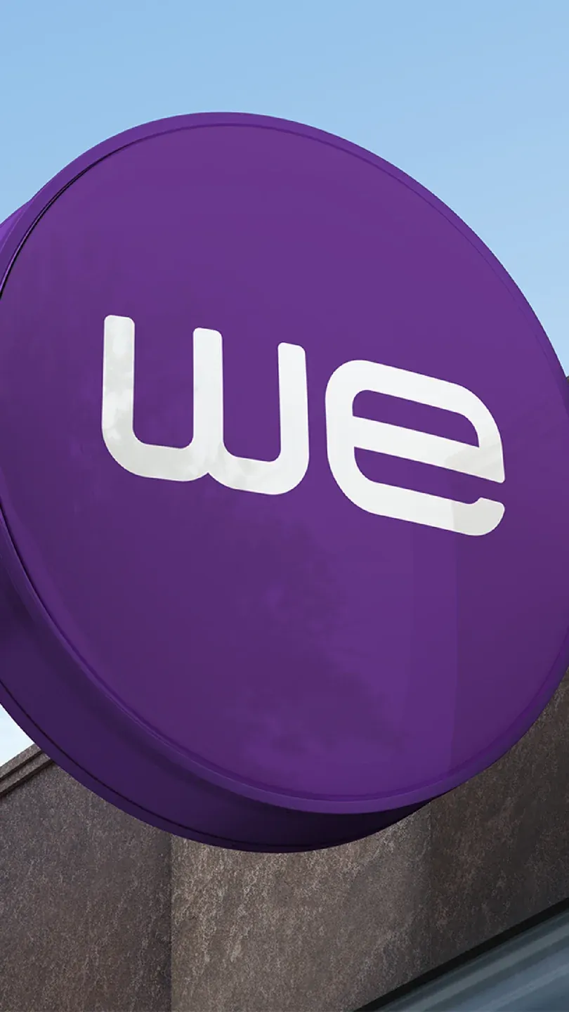 WE purple circular street sign with a white logo against the sky